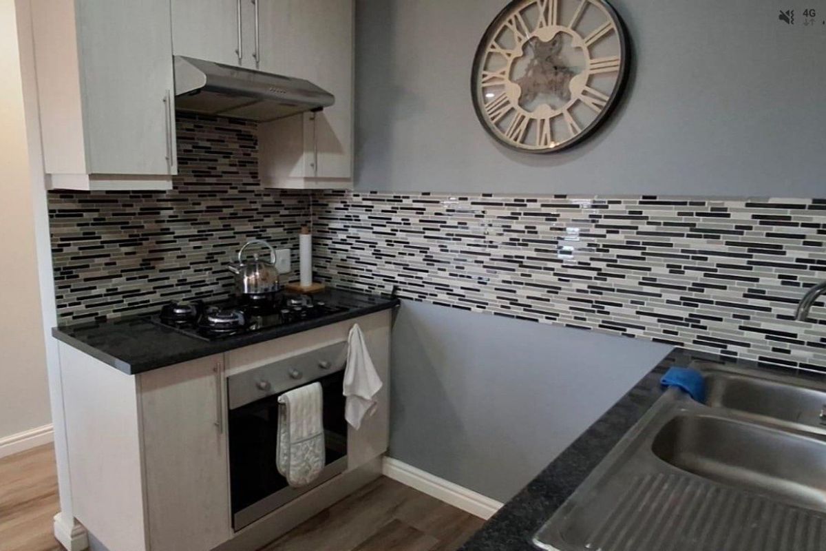 Compact kitchen featuring modern cabinetry, a gas hob with extractor fan, mosaic tile backsplash, and a double bowl sink with dark countertops.