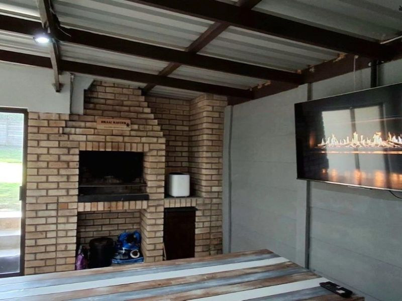 Covered outdoor patio featuring a built-in brick braai, exposed beam ceiling, and direct access to the garden through sliding glass doors.