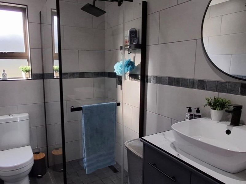 Modern bathroom featuring a glass-enclosed shower with a rain shower head, a contemporary vanity with a vessel sink, and neutral wall tiling.