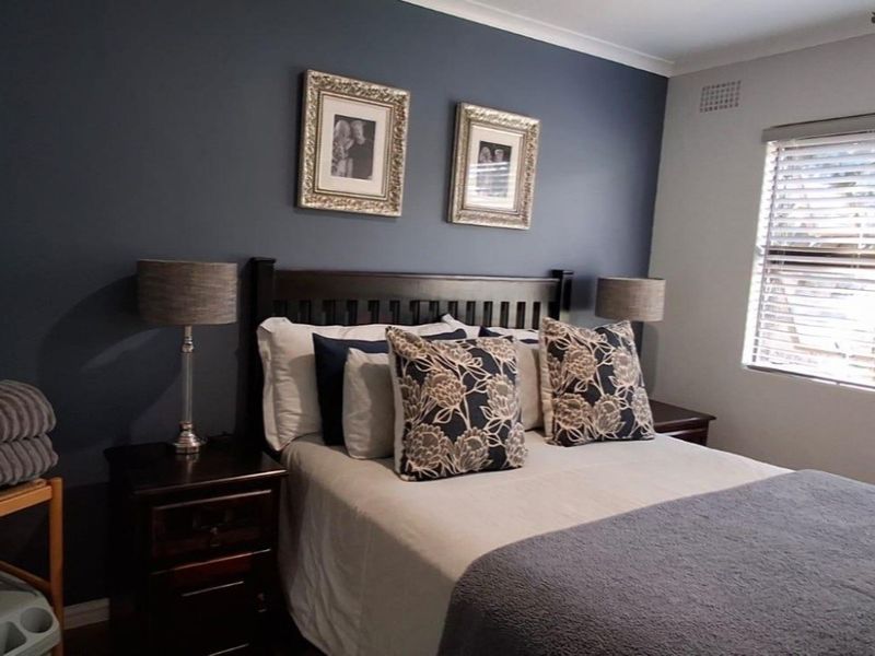 A well-maintained bedroom featuring a dark accent wall, neutral flooring, and venetian blinds for natural light control.