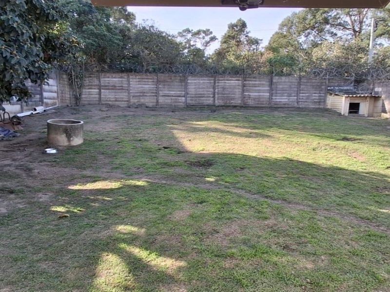 A spacious backyard featuring a precast concrete boundary wall with security razor wire and a concrete well structure.
