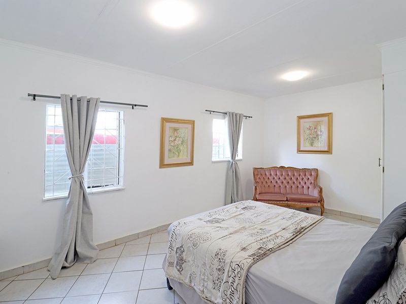 A well-lit bedroom featuring tiled flooring, security bars on the windows, and neutral wall finishes, providing a clean and functional living space.