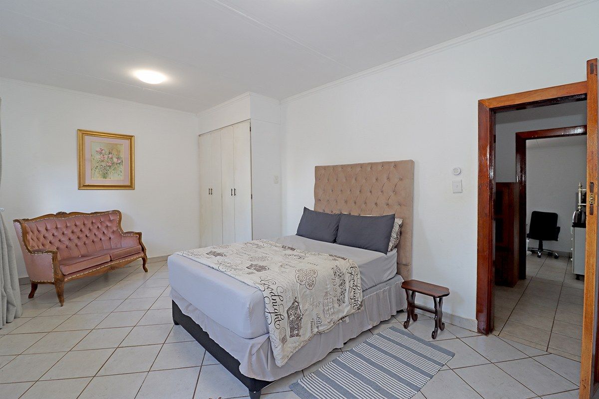 Spacious bedroom featuring tiled flooring, built-in cupboards, and coved ceiling details, offering a functional layout with direct access to an adjoining room.