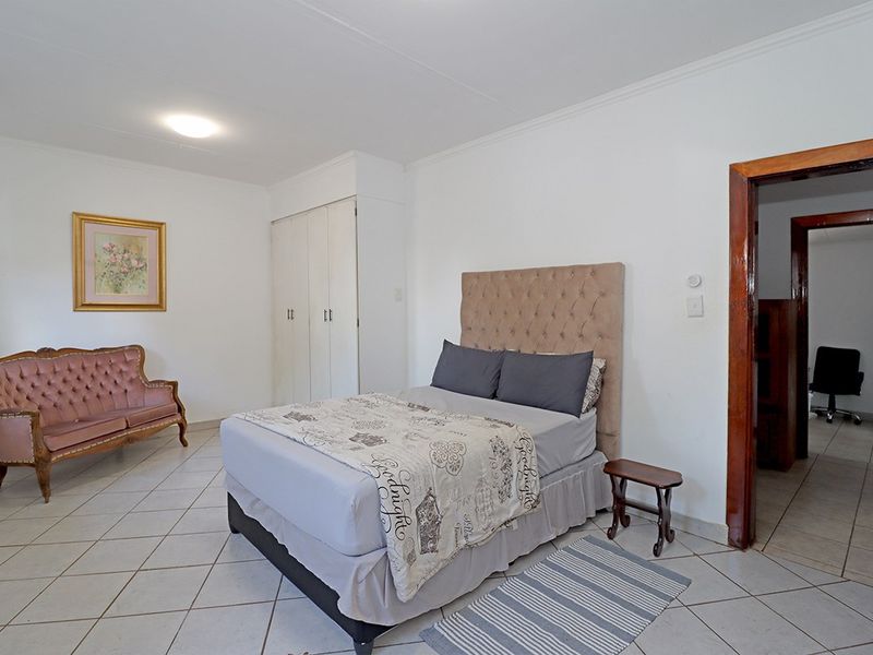 Spacious bedroom featuring tiled flooring, built-in cupboards, and coved ceiling details, offering a functional layout with direct access to an adjoining room.
