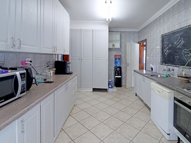 A functional kitchen featuring white cabinetry, laminate countertops, tiled flooring, and a built-in oven with hob, offering ample storage and workspace.