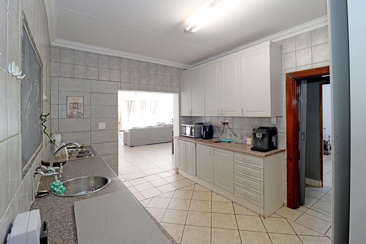 A functional kitchen featuring white cabinetry, laminate countertops, tiled splashbacks, and ceramic floor tiles, with an open flow into the adjacent living area.
