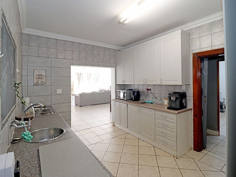 A functional kitchen featuring white cabinetry, laminate countertops, tiled splashbacks, and ceramic floor tiles, with an open flow into the adjacent living area.