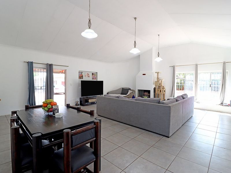 Spacious open-plan living and dining area featuring vaulted ceilings, tiled flooring, a central fireplace, and large sliding glass doors providing natural light.