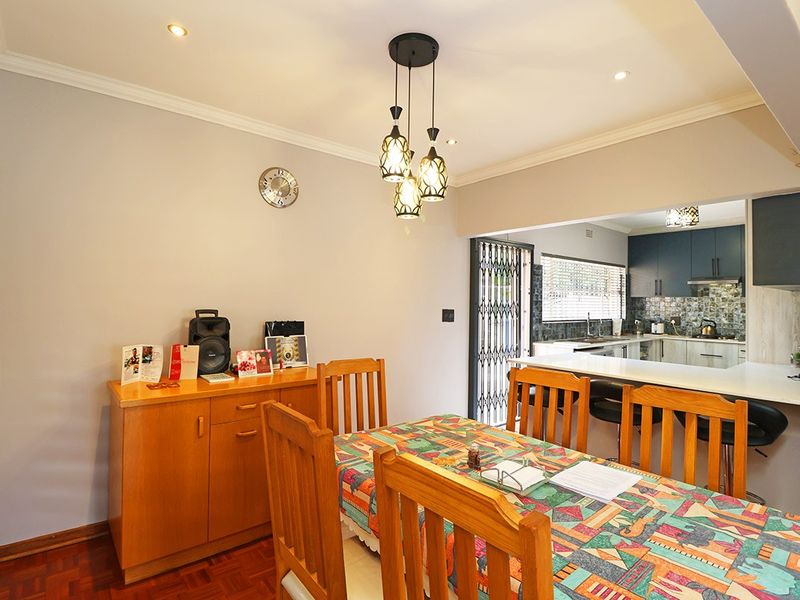 Open-plan dining area featuring parquet flooring and pendant lighting, seamlessly connected to a modern kitchen with stone countertops and ample cabinetry.