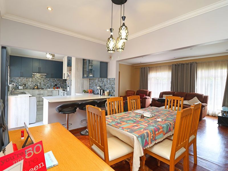 Spacious open-plan living, dining, and kitchen area featuring parquet flooring, modern cabinetry, a breakfast island, and elegant pendant lighting.