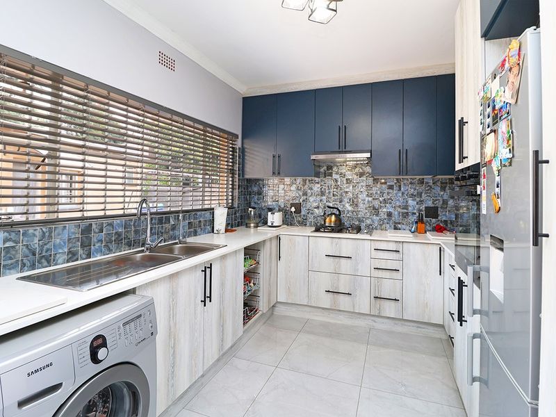 Modern kitchen featuring two-tone cabinetry, tiled backsplash, gas hob with extractor, and integrated laundry plumbing under a spacious countertop.