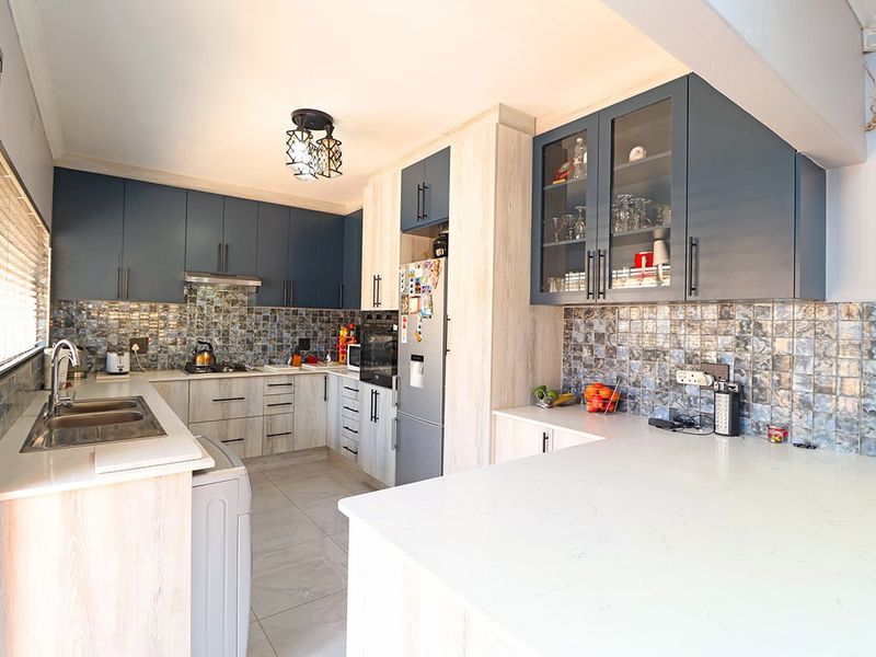 Modern kitchen featuring two-tone cabinetry, quartz countertops, mosaic tile backsplash, and integrated appliances, offering a functional and stylish cooking space.