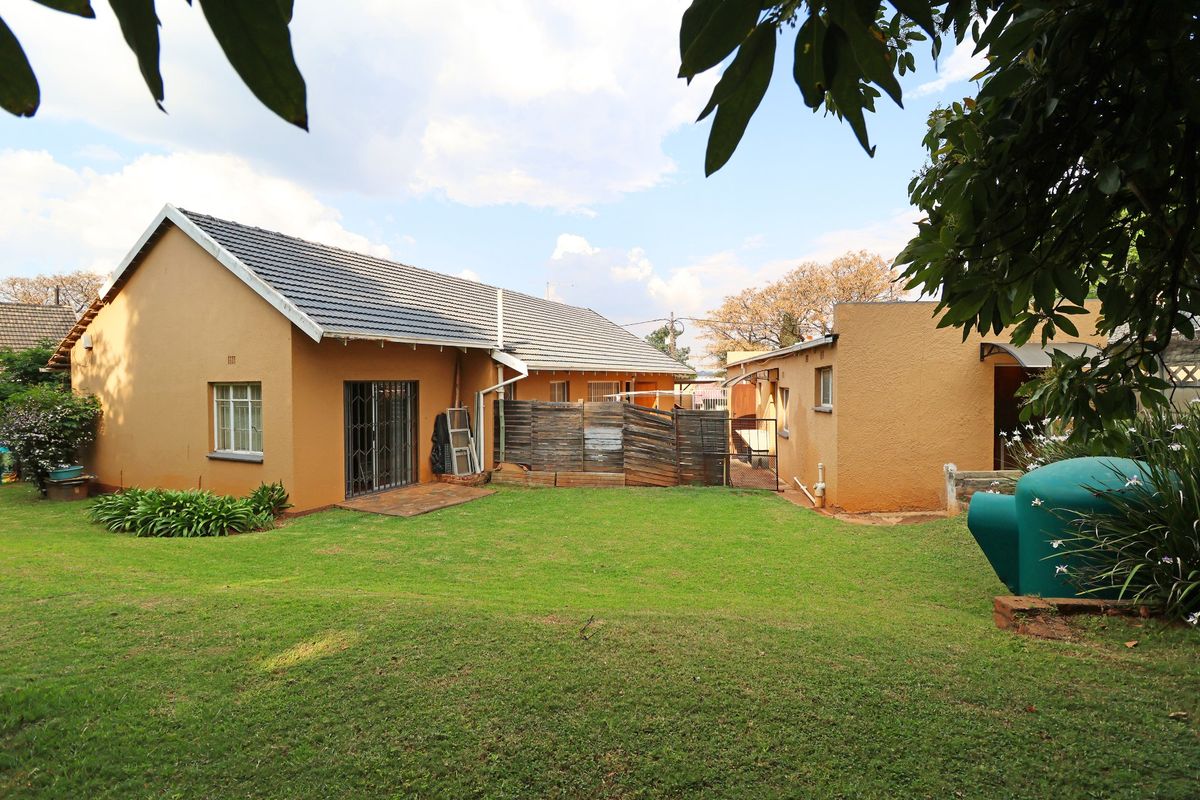 Rear view of the house featuring a spacious lawn, tiled roof, and access to the backyard via a sliding door with security gate.