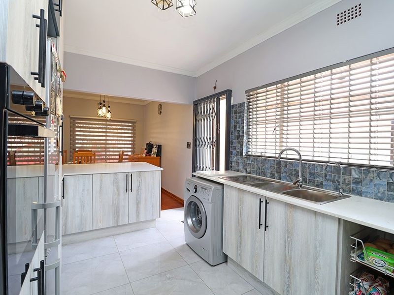 A functional kitchen featuring light wood-grain cabinetry, a double stainless steel sink, built-in oven, and tiled backsplash with direct access to the exterior.