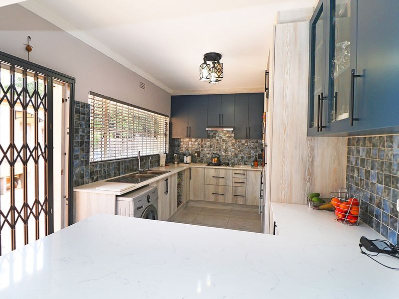 Modern kitchen featuring blue and wood-grain cabinetry, stone countertops, tiled backsplash, and integrated appliances with direct access to an outdoor area.