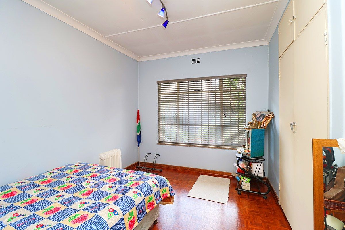A bedroom featuring parquet flooring, built-in cupboards, and venetian blinds, offering a functional space with potential for modern updates.