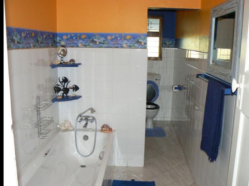 A dated bathroom featuring a built-in bathtub, separate toilet area, and ceramic tiling with a decorative border.