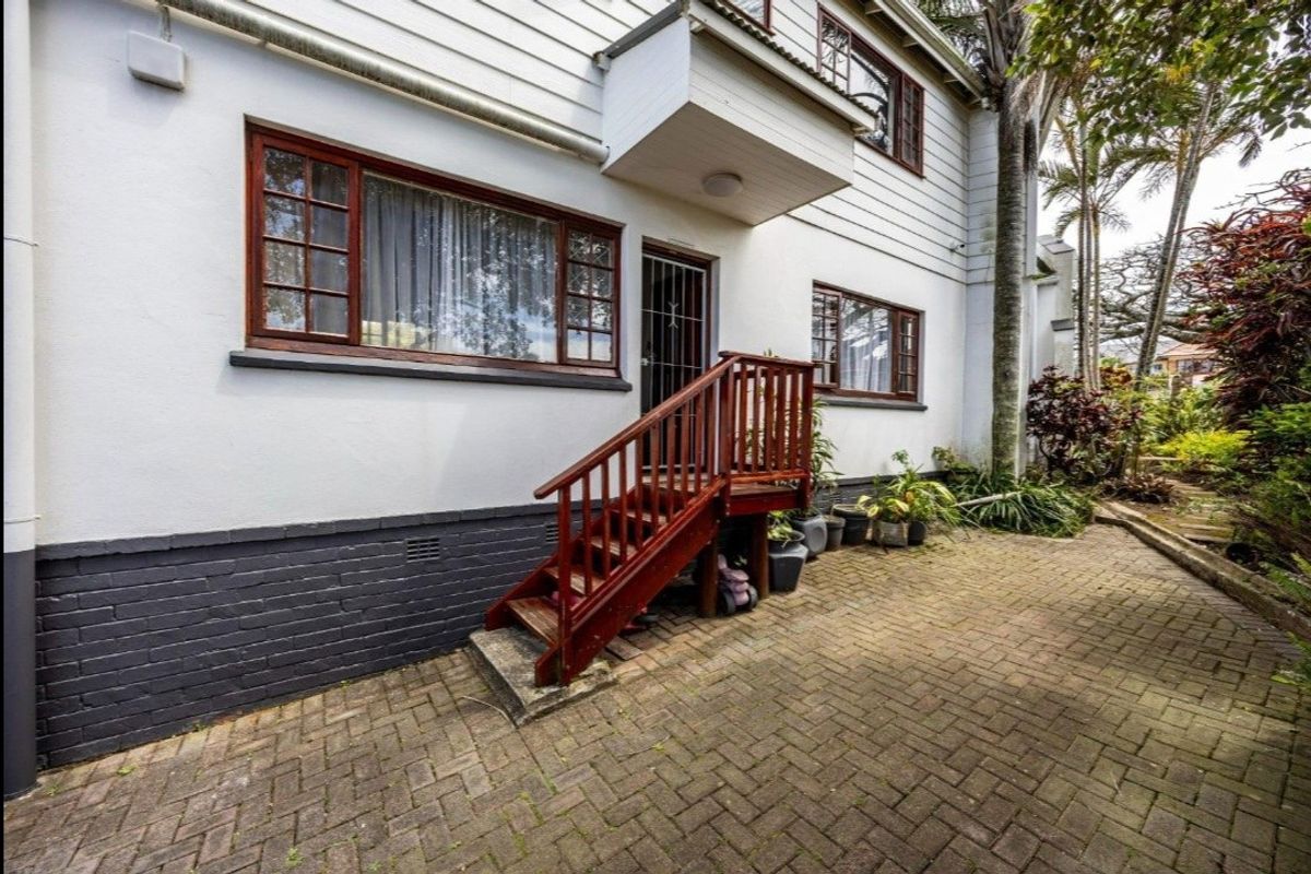 Rear exterior view of the property featuring a brick paved patio, timber staircase access, and traditional timber-framed windows set against a white painted facade.