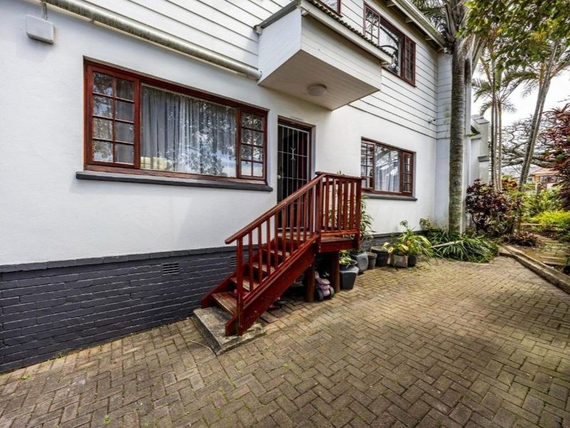 Rear exterior view of the property featuring a brick paved patio, timber staircase access, and traditional timber-framed windows set against a white painted facade.