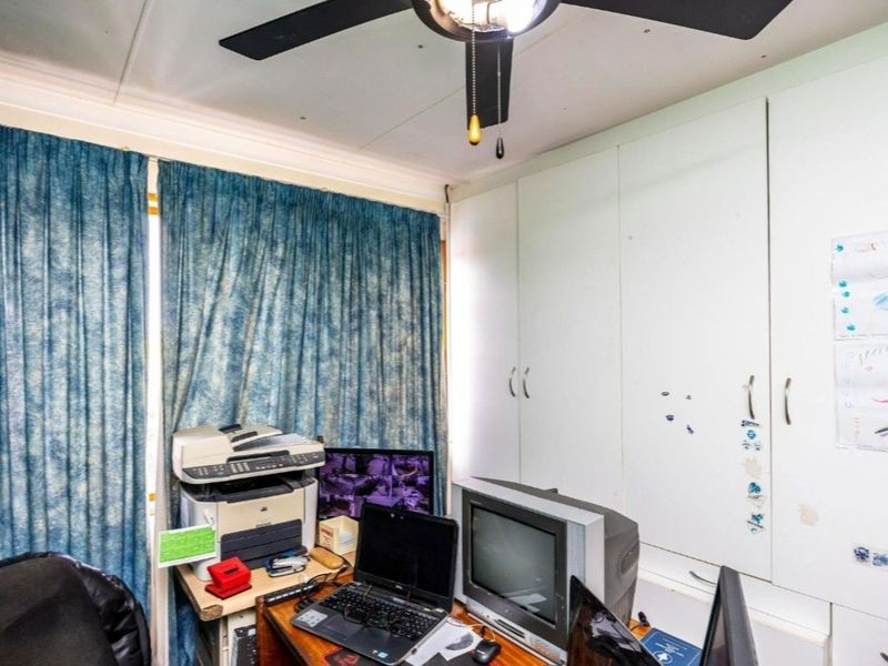 A bedroom featuring built-in cupboards and a ceiling fan, currently utilized as a home office space.