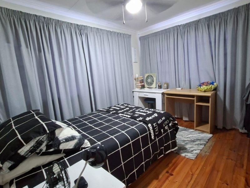 A bedroom featuring timber flooring, a ceiling fan, and built-in cupboard storage, finished with decorative ceiling cornicing.