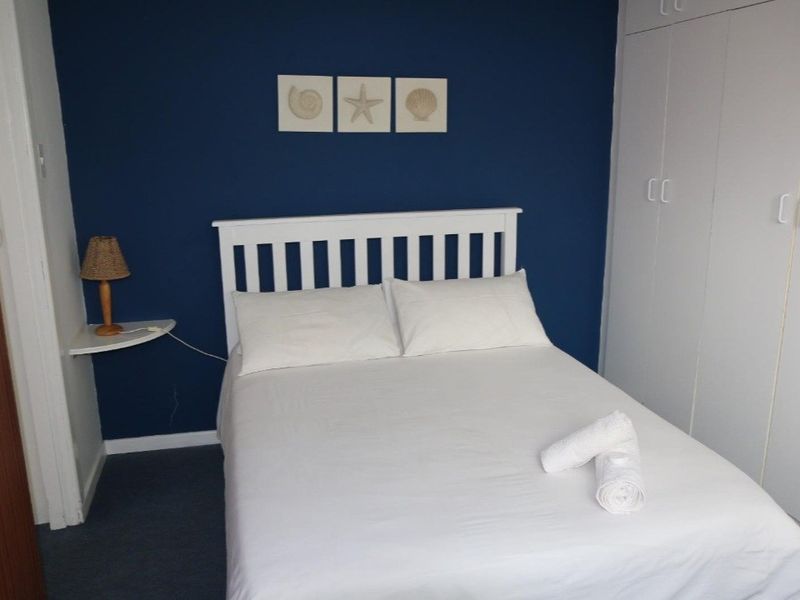 A bedroom featuring a dark blue accent wall, built-in white cupboards, and a floating bedside shelf.