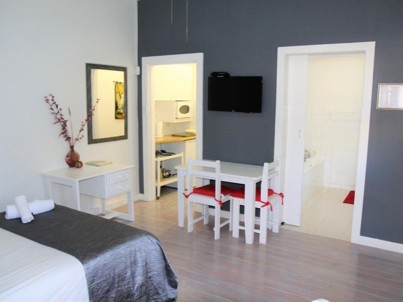 A bedroom featuring laminate flooring, a wall-mounted television, and direct access to an adjoining kitchenette and bathroom.