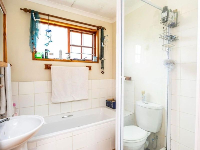 A functional bathroom featuring a pedestal basin, built-in bathtub, separate shower enclosure, and toilet with tiled splashbacks and a timber-framed window.