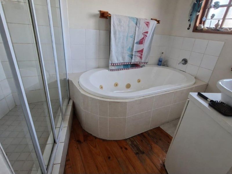 Bathroom featuring a built-in bathtub, separate shower enclosure, and basin with timber flooring and tiled wall finishes.