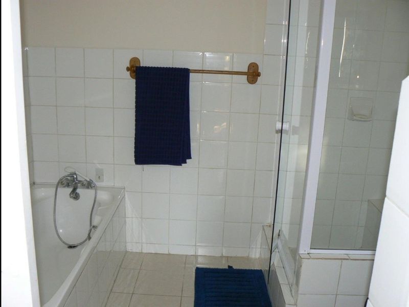 A functional bathroom featuring a built-in bathtub, a separate shower enclosure, and classic white ceramic wall and floor tiling.