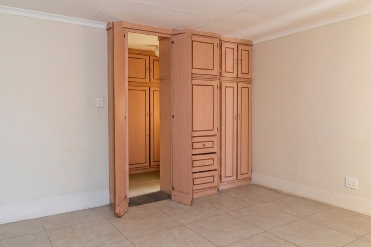 A bedroom featuring tiled flooring, coved ceilings, and integrated built-in cupboards with a walk-in storage area.