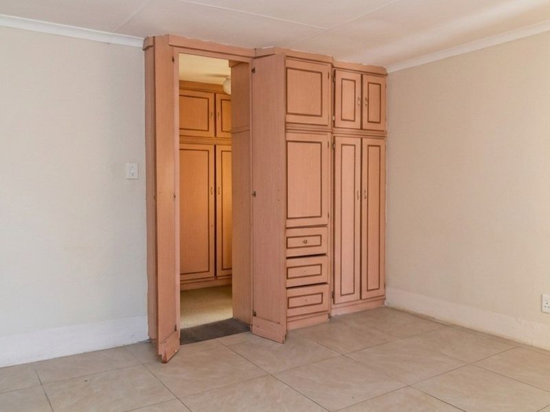 A bedroom featuring tiled flooring, coved ceilings, and integrated built-in cupboards with a walk-in storage area.