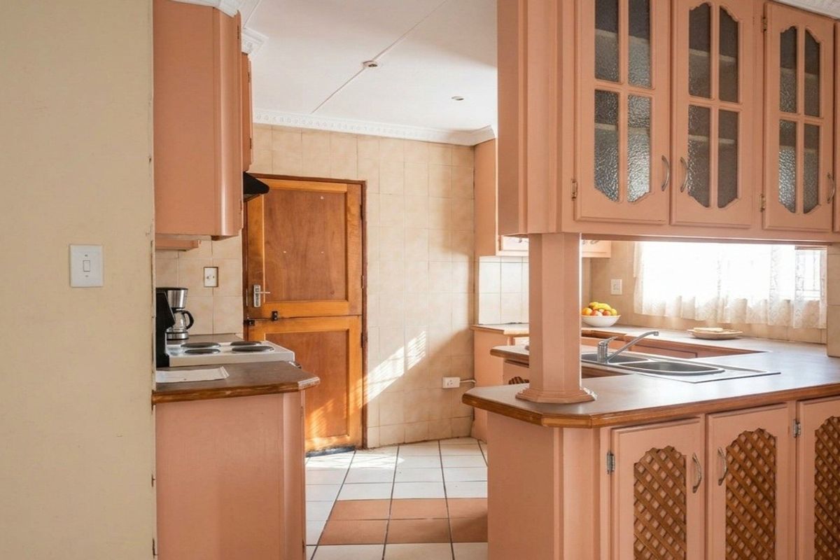 A dated kitchen featuring original cabinetry, laminate countertops, a double basin sink, and ceramic tile flooring with direct access to an exterior door.