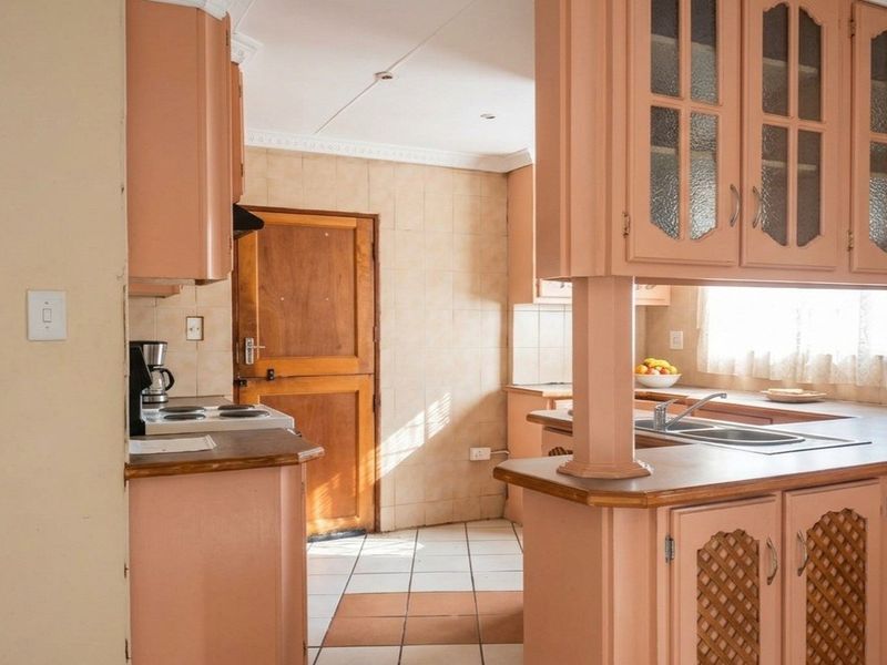 A dated kitchen featuring original cabinetry, laminate countertops, a double basin sink, and ceramic tile flooring with direct access to an exterior door.