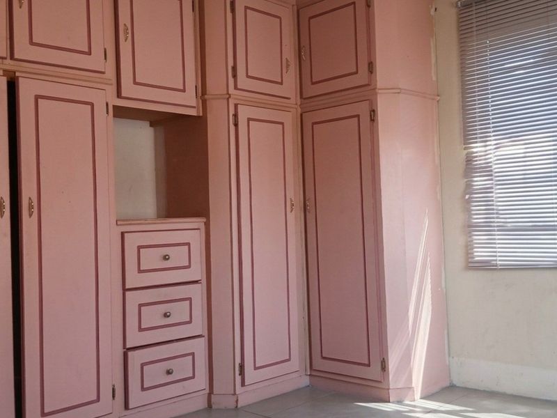Bedroom featuring extensive built-in cabinetry with a dated finish and fitted venetian blinds, offering ample storage space.