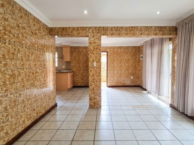 Open plan living and kitchen area featuring extensive tiled wall finishes, neutral floor tiles, and direct access to the exterior through a sliding glass door.
