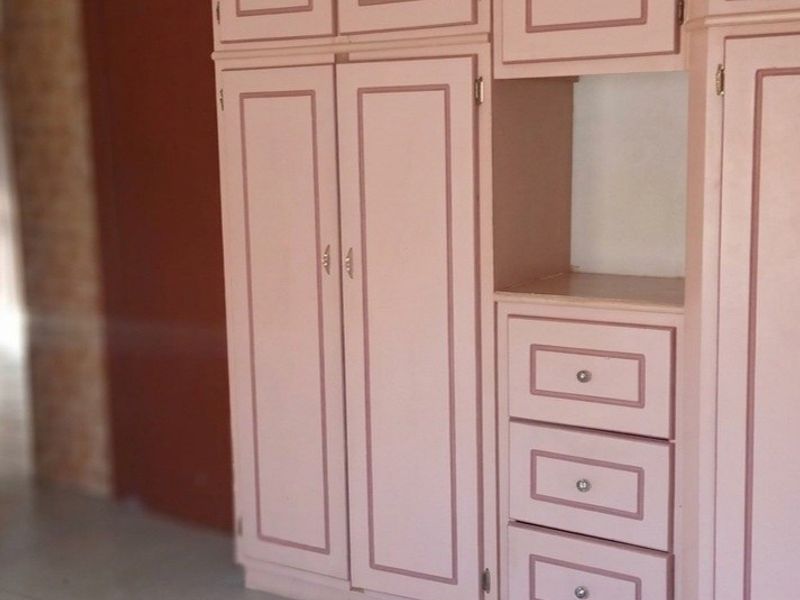 A bedroom featuring built-in cupboards with a dated pink finish and neutral tiled flooring.
