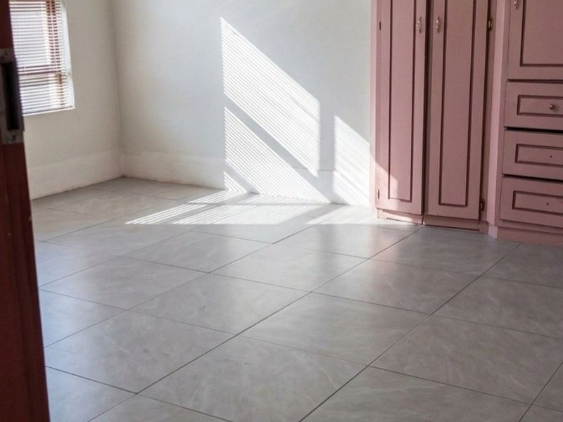 A bright, empty bedroom featuring neutral tiled flooring and built-in pink cabinetry with integrated storage.