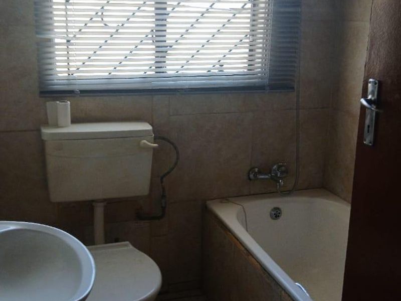 A compact bathroom featuring a bathtub, pedestal basin, and toilet with tiled finishes and a window with security bars.