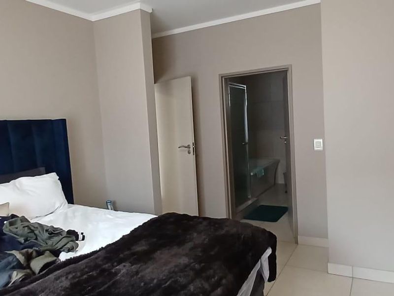 A well-maintained bedroom featuring neutral wall tones, tiled flooring, built-in cupboards, and direct access to an en-suite bathroom.