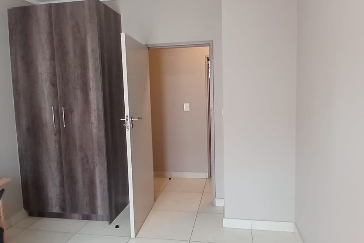 A bedroom featuring neutral wall tones, tiled flooring, and a built-in wooden wardrobe, providing a clean and functional living space.