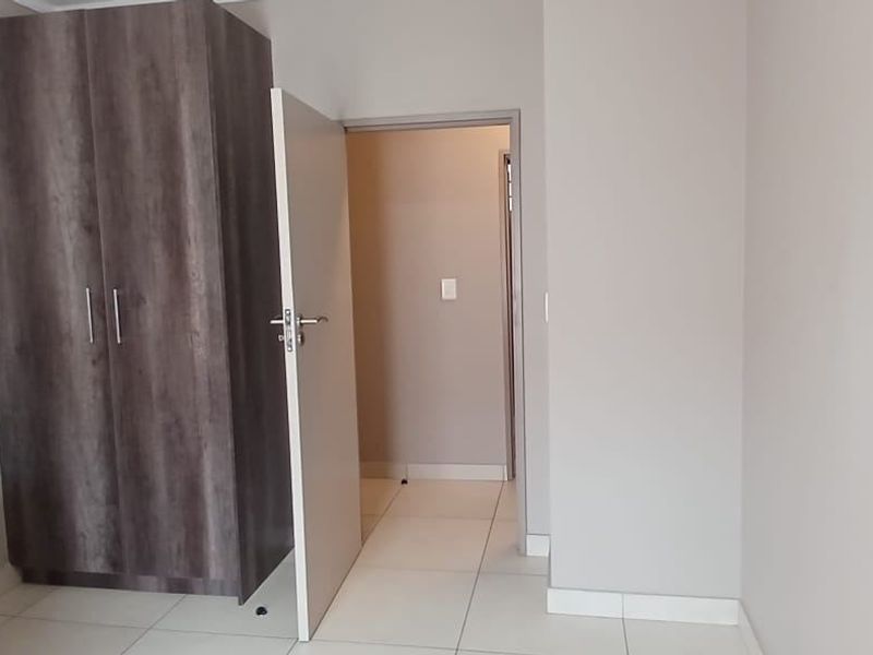 A bedroom featuring neutral wall tones, tiled flooring, and a built-in wooden wardrobe, providing a clean and functional living space.