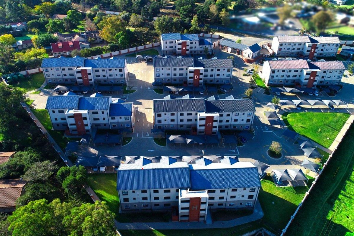 Aerial view of a residential apartment complex featuring multiple multi-story buildings, paved parking areas with carports, and surrounding landscaped green spaces.