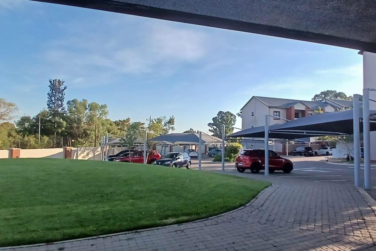 View of the apartment complex exterior featuring a paved driveway, covered parking bays, and a well-maintained communal lawn area.