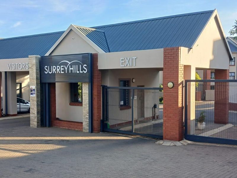 The entrance and exit gatehouse of the Surrey Hills apartment complex, featuring brick pillars, metal roofing, and secure access gates.