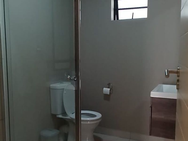 A modern bathroom featuring a glass-enclosed shower, a wall-mounted vanity with a basin, and neutral tiled flooring.