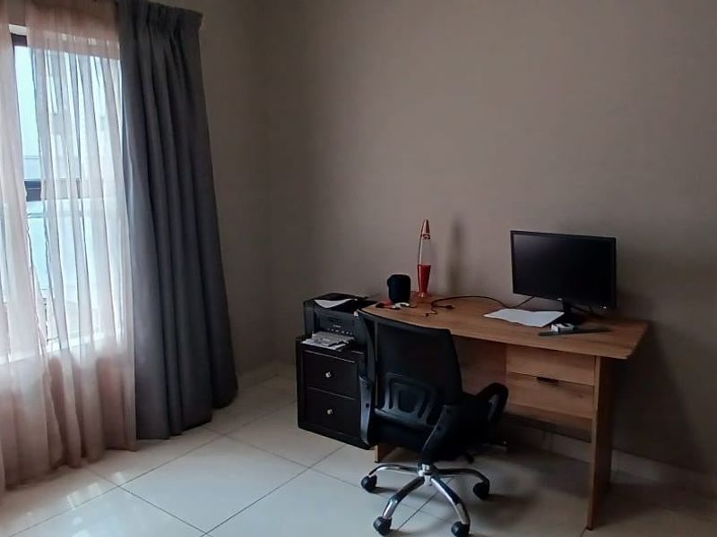 A functional bedroom space featuring neutral wall tones and tiled flooring, currently utilized as a home office area.