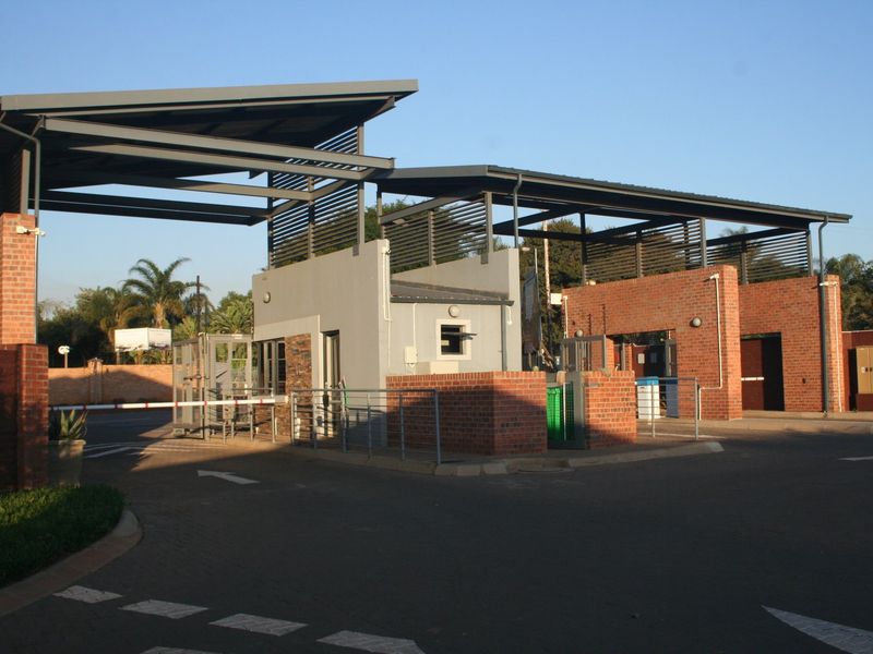 A modern security gatehouse entrance featuring brick masonry, metal roofing, and automated boom gates for controlled access to the property.