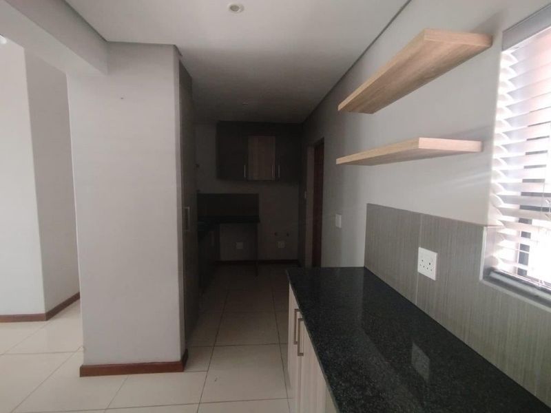 A modern kitchen featuring granite countertops, built-in cabinetry, and floating shelves, finished with neutral tiled flooring and recessed lighting.