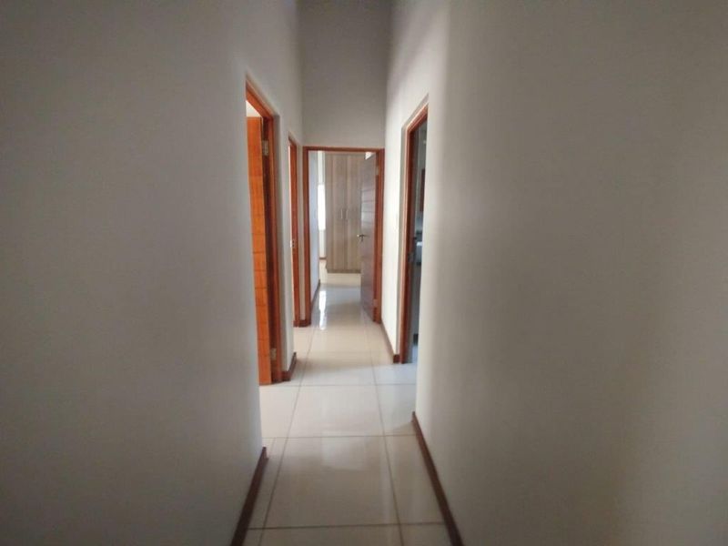 A clean, well-lit hallway featuring neutral tiled flooring and wooden door frames, providing access to multiple rooms within the townhouse.
